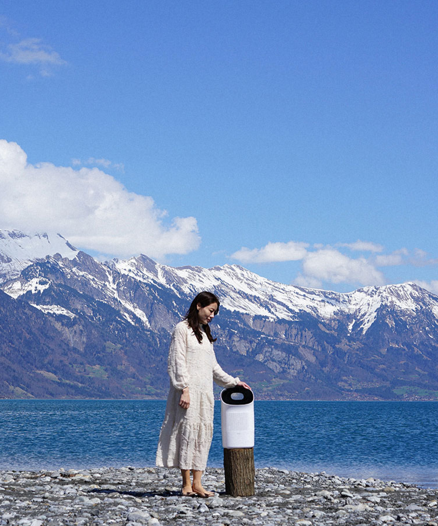 Woman standing on pebble beach next to Zenwell Super Air Purifier + Humidifier in front of alpine lake